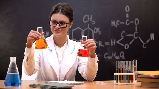 Female scientist comparing flasks with colored liquid, detergent laboratory - Фото, зображення