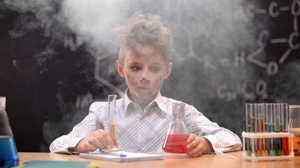 Dirty schoolboy holding chemistry equipment, explosion during experiment - Foto, Imagen