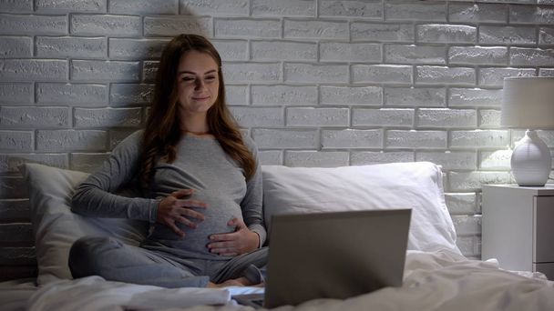 Happy pregnant woman stroking tummy, watching educational videos on internet - Фото, зображення