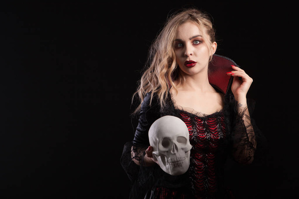 Increíble chica muerta vestida como vampiro sosteniendo un cráneo para el carnaval de Halloween
 - Foto, Imagen