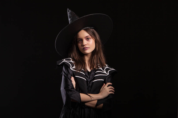 Kleine Hexe mit schwarzem Kleid, die mit ernstem Gesichtsausdruck in die Kamera blickt - Foto, Bild