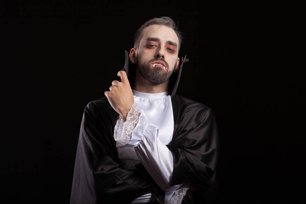 Attractive young Dracula keeping his arms crossed with his teeth out for halloween - Фото, изображение