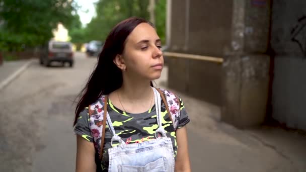 A beautiful young woman in casual clothes is smiling in the street. The long hair brunette develops in the wind in slow motion. - Video