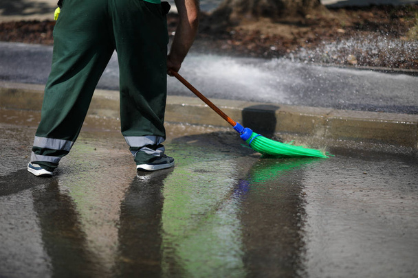 Ο καθαριστής δρόμων καθαρίζει το πεζοδρόμιο της πόλης με νερό από σωλήνα και - Φωτογραφία, εικόνα