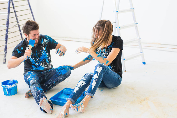 Renovation, redecoration and interiors concept - Young couple sitting on the white floor and pour paint and having fun - 写真・画像