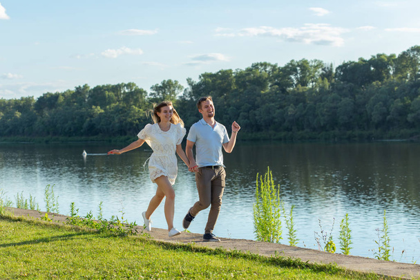 Amor y concepto de relación - El hombre y la mujer felices corriendo en un parque cerca de un lago
 - Foto, imagen