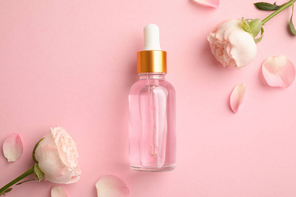 Flat lay composition with rose essential oil and flowers on pink background - 写真・画像