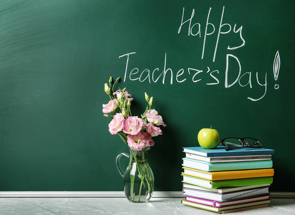 Green chalkboard with inscription HAPPY TEACHER'S DAY, vase of flowers and books on grey stone table. Space for text - Fotografie, Obrázek