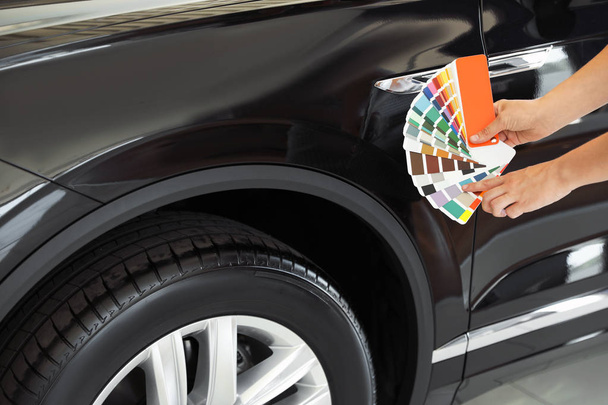 Young woman holding palette with color samples near black car, closeup - Foto, Bild