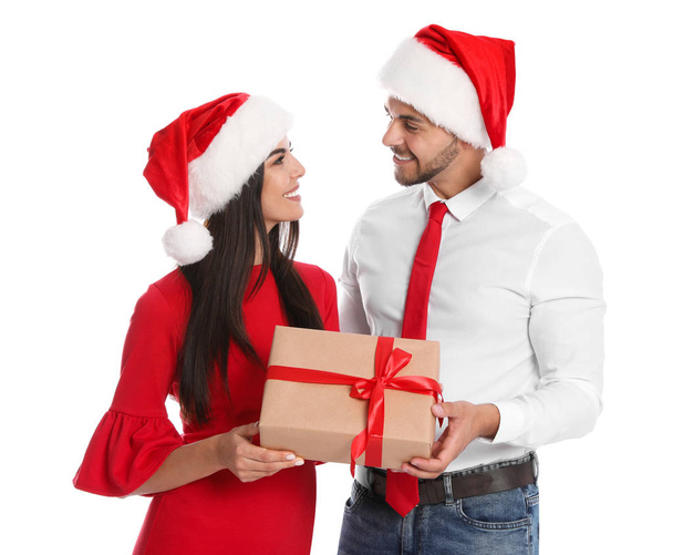 Lovely young couple in Santa hats with gift box on white background. Christmas celebration - Zdjęcie, obraz