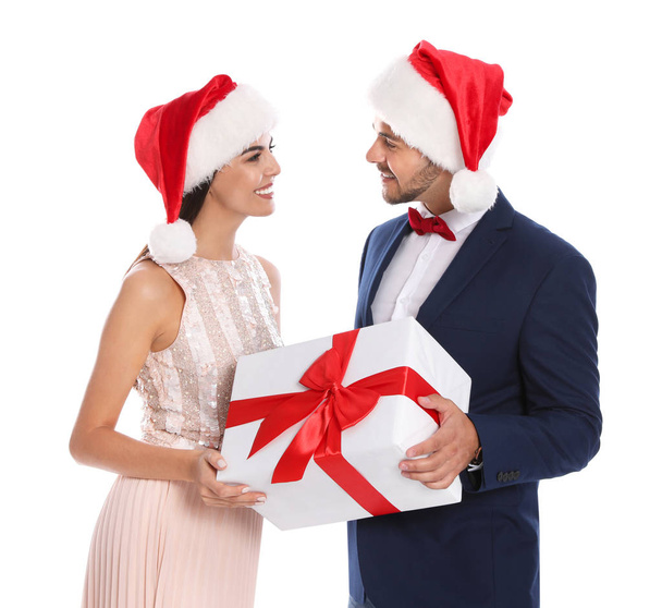 Lovely young couple in Santa hats with gift box on white background. Christmas celebration - Fotografie, Obrázek