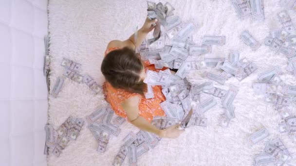 Een mooi meisje geniet van een enorme rijkdom. vrouwen sorteren veel bankbiljetten op een wit bed, gooit geld, Slow Motion, bovenaanzicht - Video
