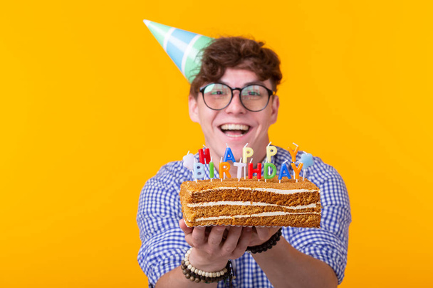 Funny positive guy holds in his hands a homemade cake with the inscription happy birthday posing on a yellow background. Concept of holidays and anniversaries. - Foto, immagini