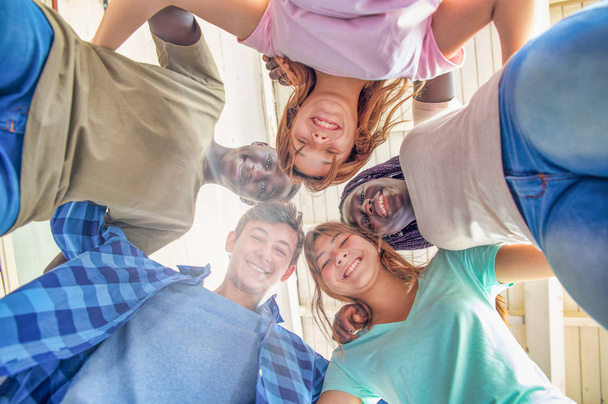 Blick nach oben auf eine multiethnische Gruppe glücklicher Teenager, die in die Kamera lächeln. - Foto, Bild