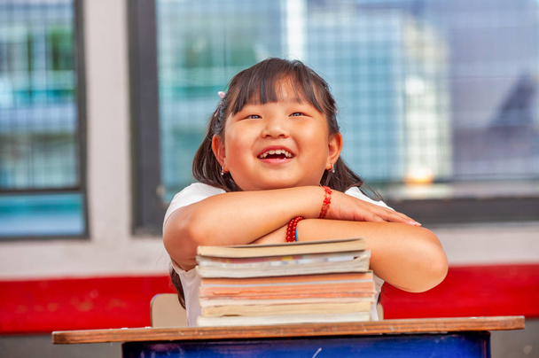 Feliz chica asiática con sus manos sobre los libros en la escuela
 - Foto, imagen