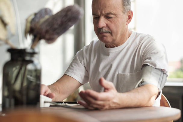 Homem usando máquina de pressão arterial em casa para verificar suas estatísticas vitais
. - Foto, Imagem
