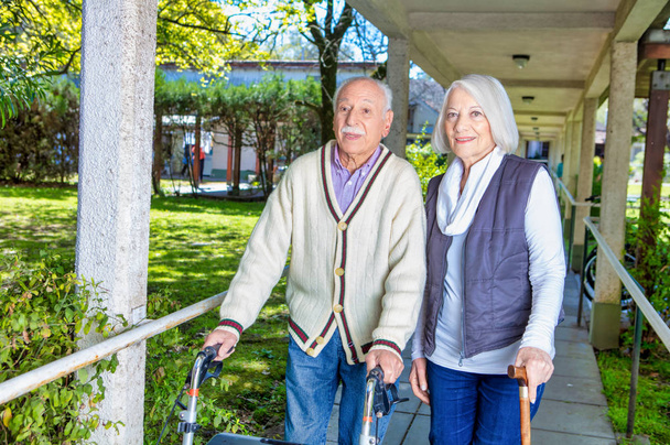 Heureux couple retraité avec bâton et marcheur dans le jardin. - Photo, image
