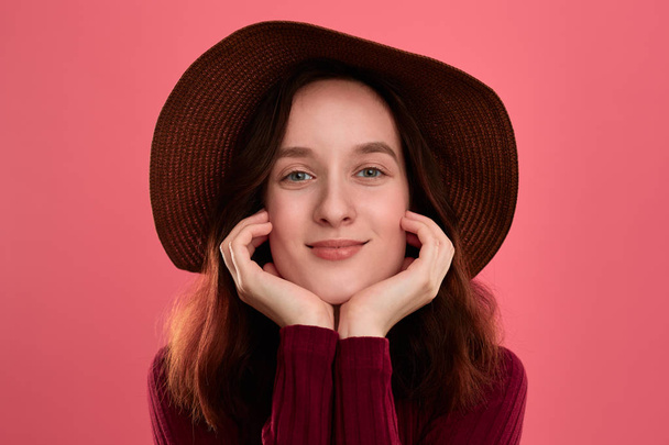 Retrato de cerca de una hermosa chica morena feliz con un sombrero de ala ancha posando sobre un fondo rosa oscuro
. - Foto, Imagen