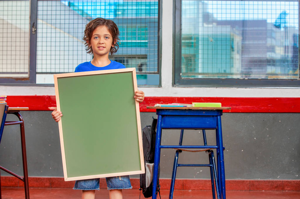 Młody chłopak w szkole trzyma zieloną tablicę. - Zdjęcie, obraz