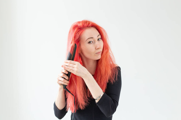 Coiffure, coiffeur et concept de personnes - élégante femme aux cheveux roux avec fer à friser sur fond blanc
. - Photo, image