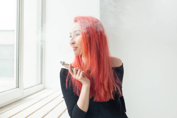 Jeugd en verslaving concept-jonge roodharige vrouw roken Vape in de buurt van het raam - Foto, afbeelding
