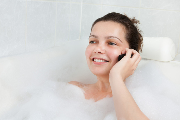 Young woman in bathtub talking on mobile - Fotoğraf, Görsel