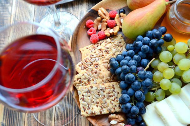 Red wine in glasses and snacks for wine on a wooden platter: cheese, nuts, crackers, pears, honey, grapes - Fotó, kép