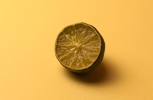The concept of ugly fruits and citrus fruits. Half of the sliced lime has dried up, deteriorated on a beige background. Selective focus with a hard shadow. Mold on citrus fruits. Copy space. - Photo, Image