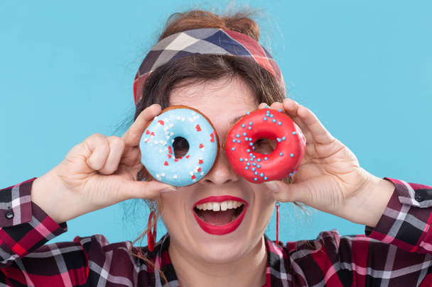 ダイエット、デザート、ジャンクフード - 青い背景にドーナツを持つピンナップかわいい女性のクローズアップ - 写真・画像