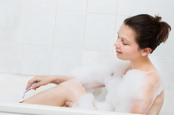 Woman in bathtub shaving her leg - Foto, Imagen