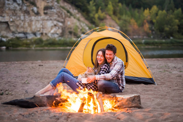 personas, turismo de verano y el concepto de la naturaleza - pareja cerca de fuego del campamento de calentamiento visto desde la tienda de campaña
 - Foto, Imagen