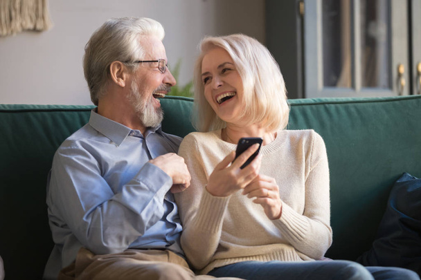 Happy retirees family laughing using smartphone at home. - Foto, Imagen