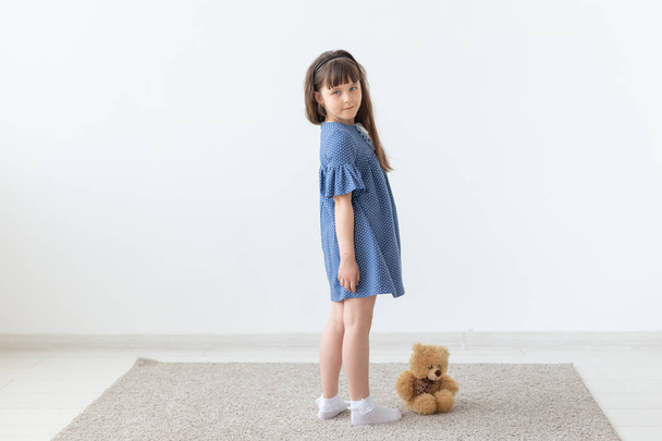 Kind meisje in blauwe jurk met speelgoed in witte kamer - Foto, afbeelding