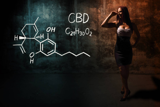 Sexy meisje of secretaresse of vrouwelijke student presenteert hand getekende chemische formule van CBD - Foto, afbeelding