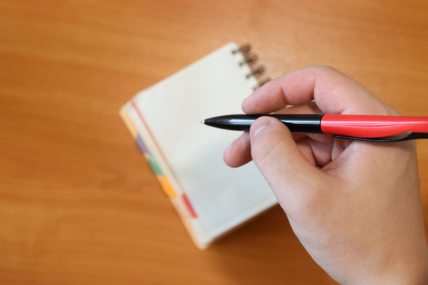 Ręka trzyma długopis. Człowiek robi notatkę w Notatniku. Tło jest poza fokusem. Praca papierowa. - Zdjęcie, obraz
