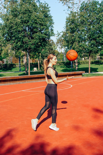 Young woman with fit body playing basketball and having fun on court. Sunny day. - 写真・画像