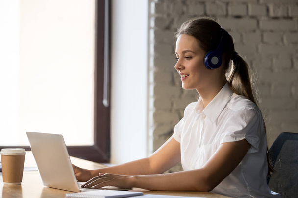 Smiling businesswoman wearing headphones using laptop at work - Foto, Imagem