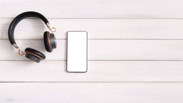 Smartphone con pantalla en blanco y auriculares inalámbricos sobre fondo de madera
 - Foto, Imagen