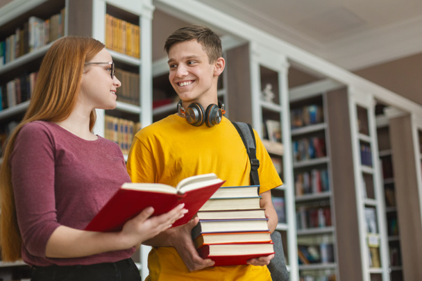 Bonito casal adolescente discutindo livro na biblioteca
 - Foto, Imagem