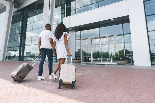 Glückliches afrikanisches Brautpaar betritt Flughafengebäude mit Gepäck - Foto, Bild