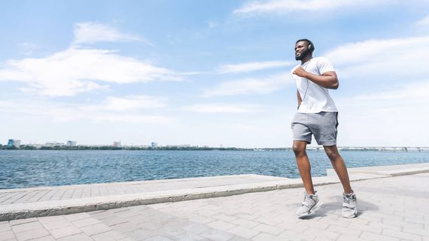afroamericano ragazzo in cuffie jogging lungo fiume in città
 - Foto, immagini