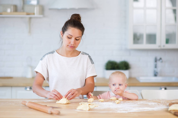 мати скульптури пироги, стоячи біля стільниці на кухні, і маленька дочка поблизу їсть тісто
 - Фото, зображення