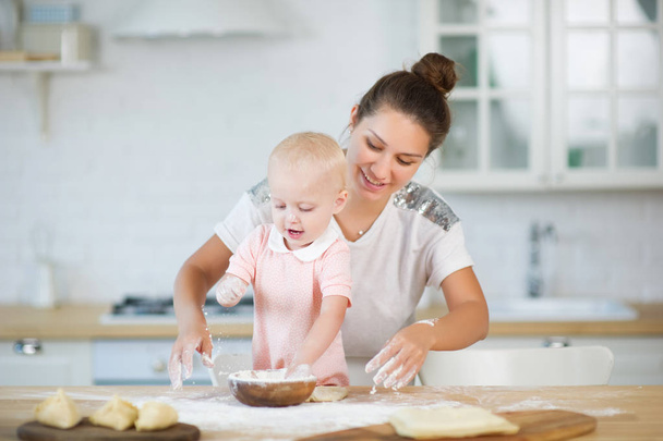 mom and her little daughter are playing cooks in the kitchen, sprinkling flour - Фото, зображення