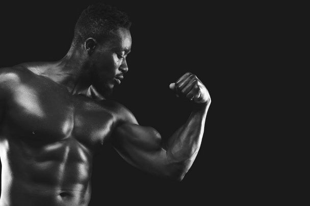 Monochrome photo of african fitness model demonstrating his strong arm - Zdjęcie, obraz