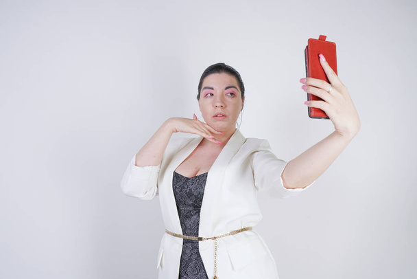 чарівна мікс гонка плюс розмір жінки в білій діловій куртці робить селфі фотографію з смартфоном в руці на білому тлі в студії
 - Фото, зображення