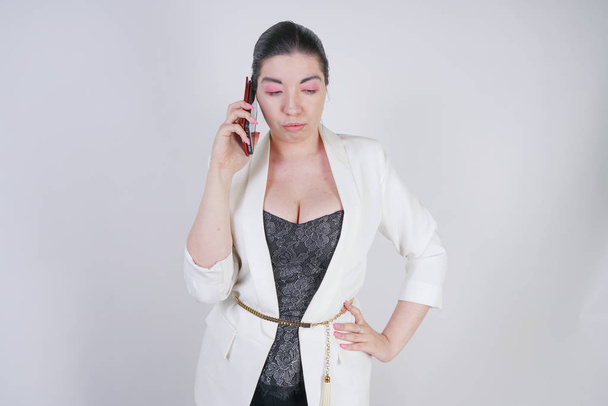 viehättävä yhdistelmä rotu plus koko nainen valkoinen liike takki seisoo onneton ja surullinen älypuhelin kädessä valkoisella taustalla Studio
 - Valokuva, kuva