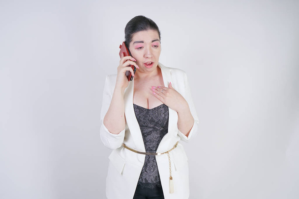 encantadora mezcla de raza más mujer de tamaño en una chaqueta de negocios blanca de pie infeliz y triste con el teléfono inteligente en la mano sobre fondo blanco en Studio
 - Foto, imagen
