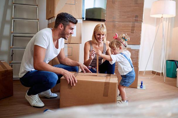 Happy parents with child moving in new home unpacking boxes - 写真・画像