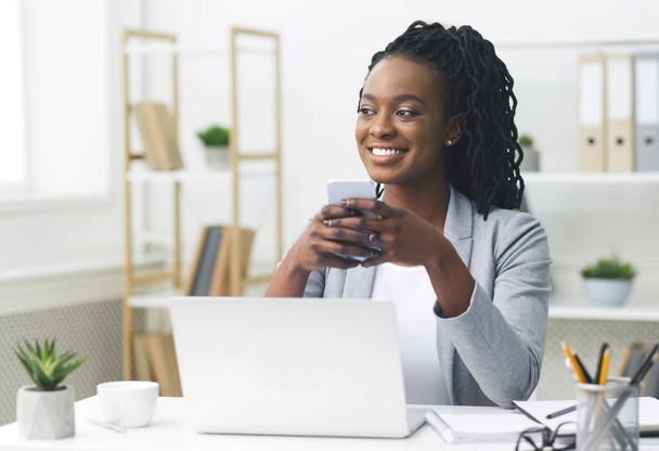 Афроамериканская предпринимательница переписывается по мобильному телефону в современном офисе
 - Фото, изображение