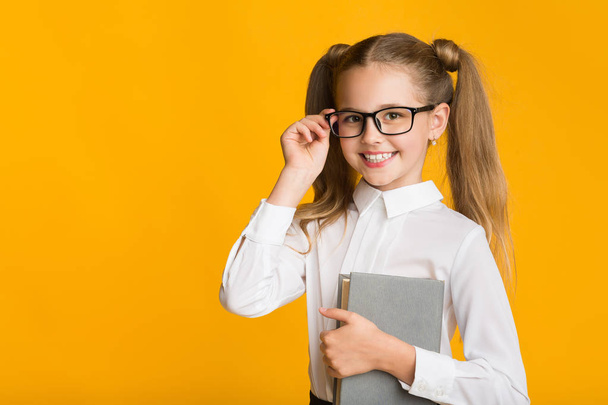 Gülümseyen Birinci Sınıf Öğrencisi Kız Sarı Arka Planda Poz Veren Kitap Tutuyor - Fotoğraf, Görsel